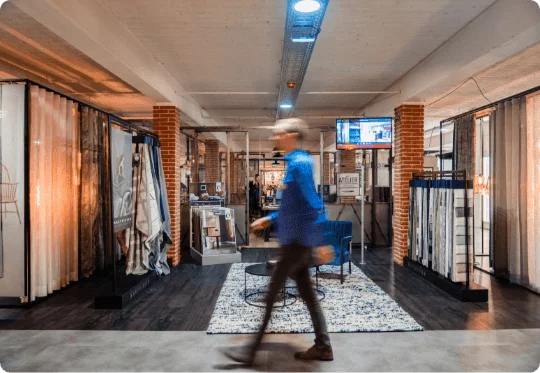 Een interieuradviseur van Poels Wonen & Slapen loopt langs de raambekleding van het Atelier.